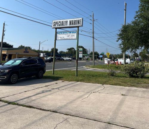Roadside sign for an appliance store beside a street, with a parked black SUV and clear blue sky.