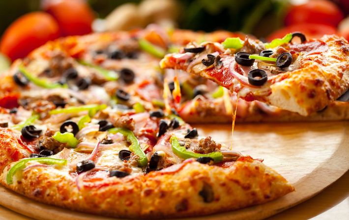 A pizza with a slice taken out of it is on a wooden cutting board.