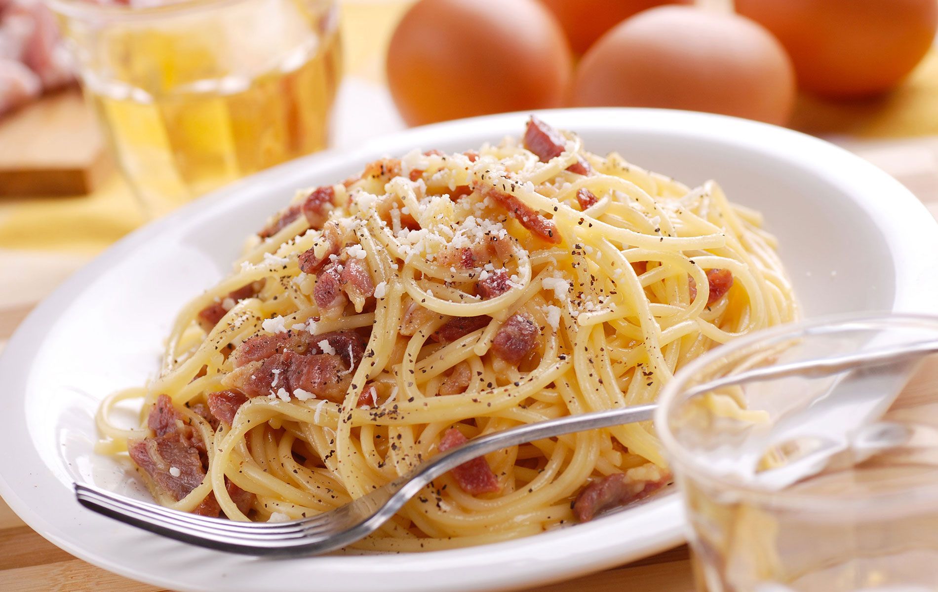 A plate of spaghetti with a fork and eggs in the background