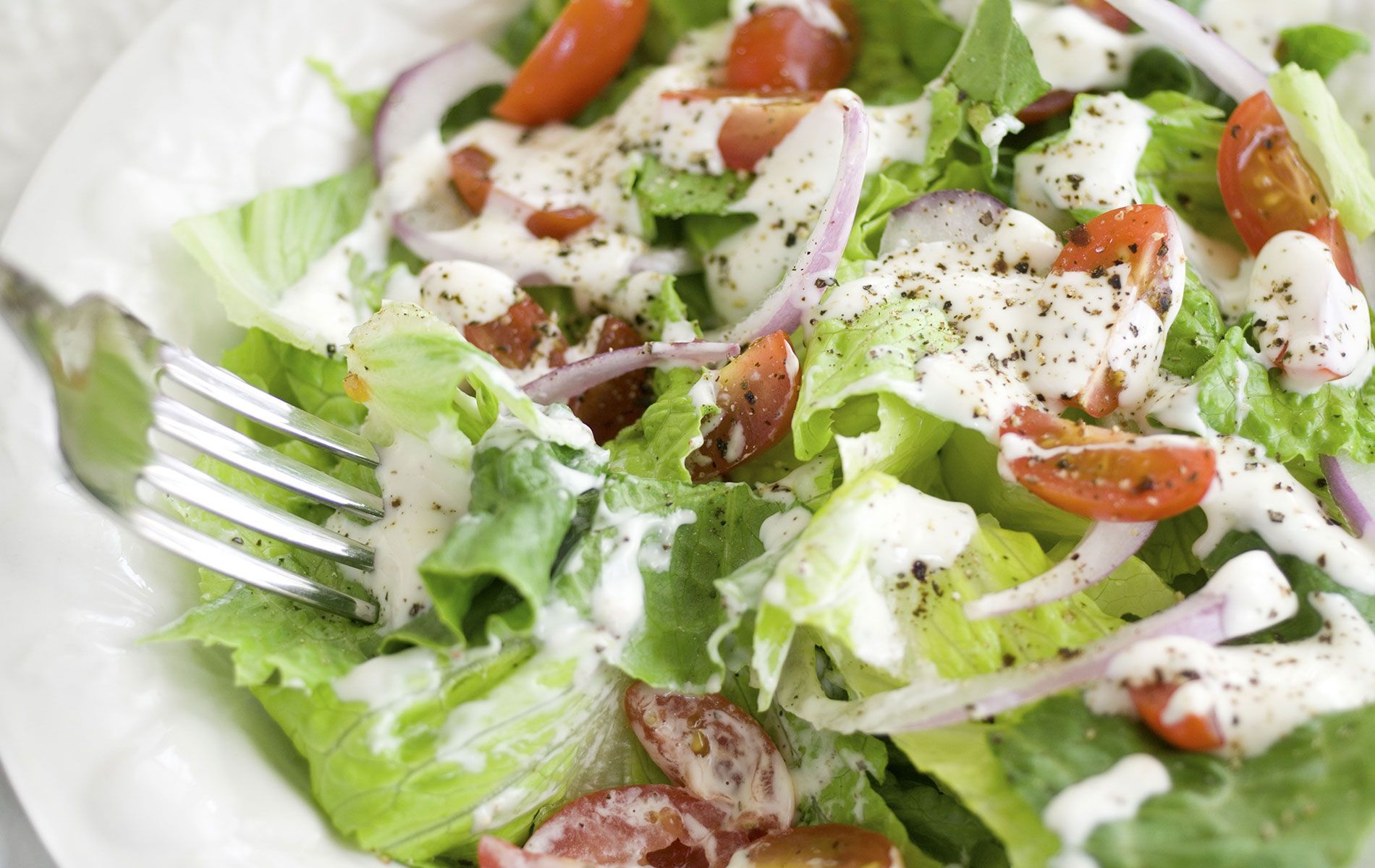 A salad with lettuce , tomatoes , onions and ranch dressing on a plate with a fork.