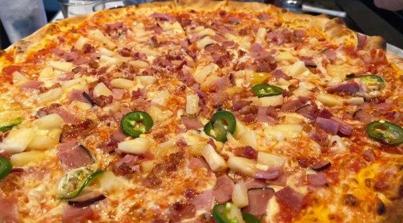 A pizza with cheese and tomatoes on a plate on a wooden table.