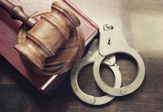 Wooden gavel, book, and silver handcuffs on a wooden surface.