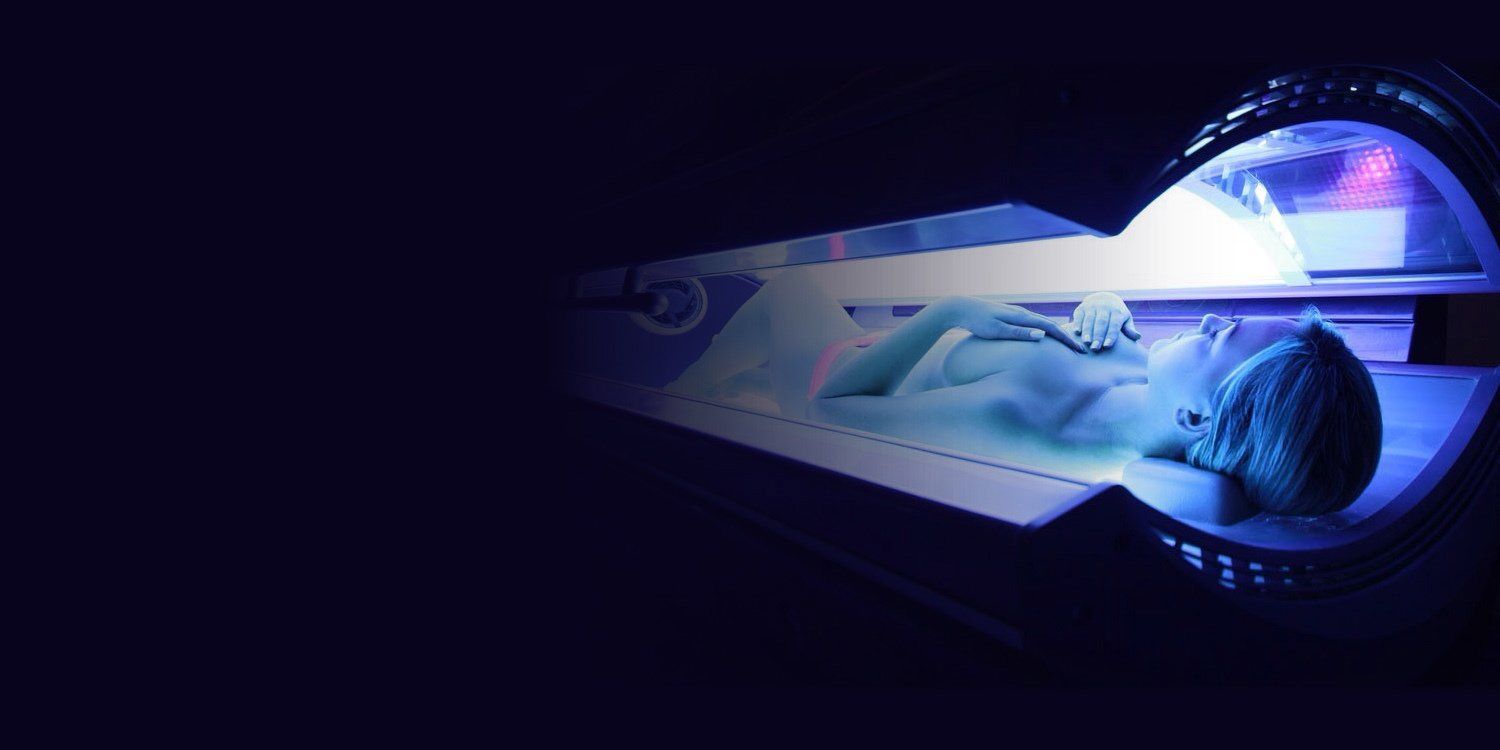 A person lies inside a blue-lit tanning bed.
