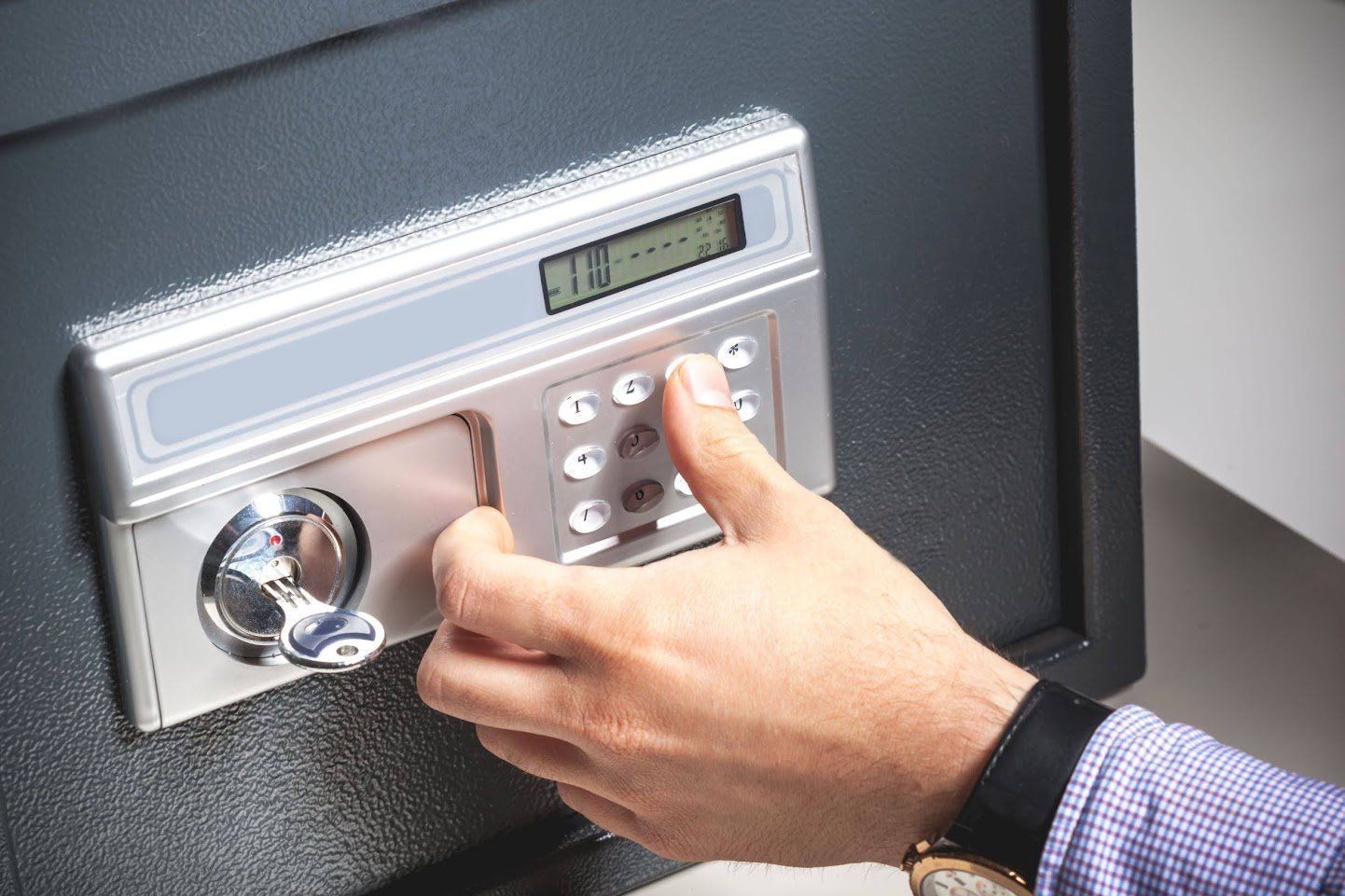 Hand entering code on a digital safe keypad. Silver and black safe, watch visible.