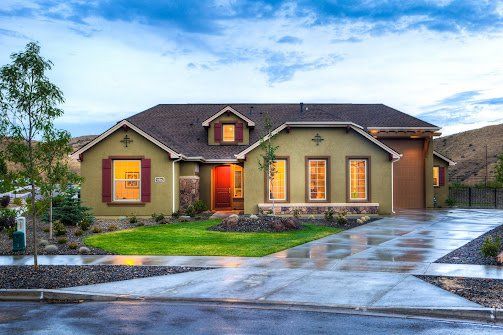 Tan house with red accents, front lawn, and driveway. Cloudy sky above.