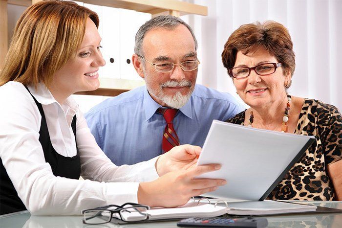 A woman reviewing paperwork with an elderly couple in an office. They appear to be discussing finances.
