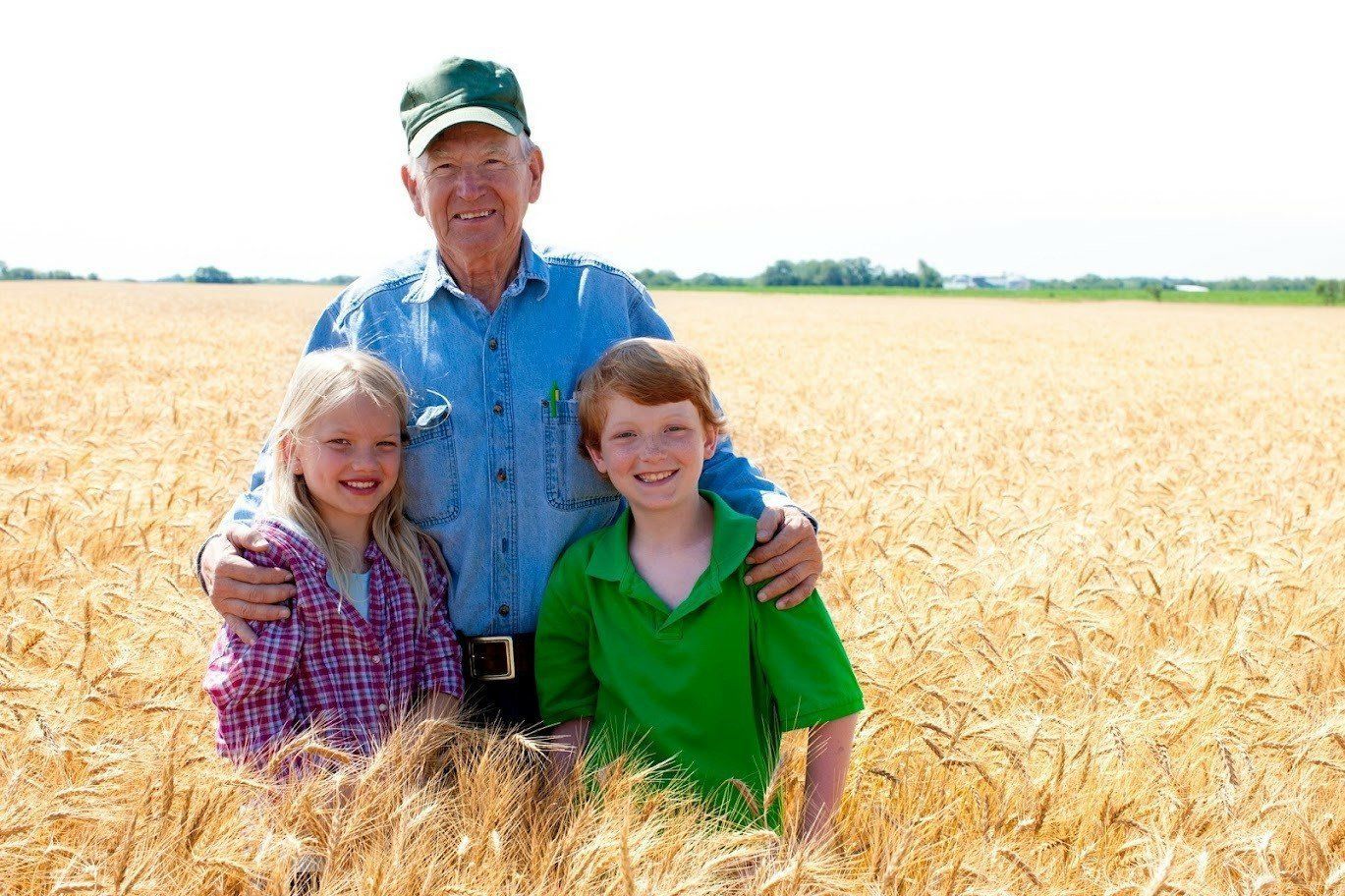 Farmer with two children in a wheat field, smiling, sunny day.