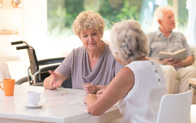 Two older adults chatting at a table in a bright care facility lounge