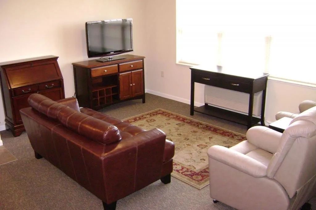 Living room with brown sofa, beige recliner, TV stand, rug, and console table by a bright window