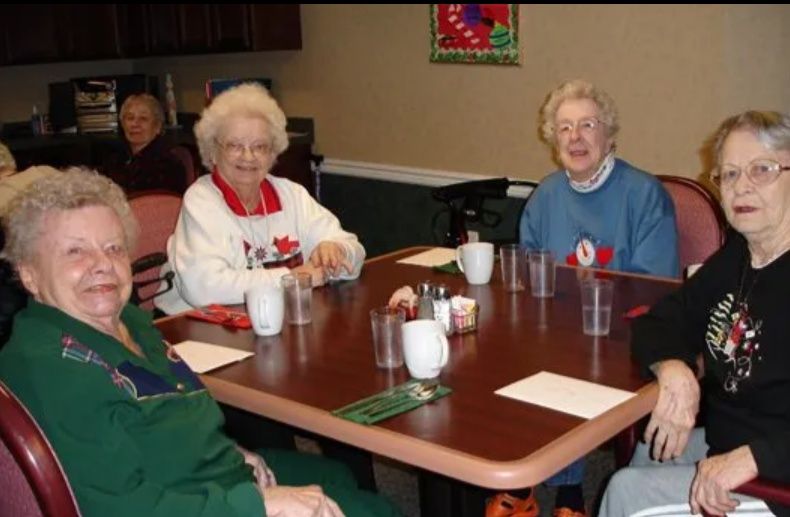 Four women sitting at a table in a dining room, chatting with cups and napkins on the table