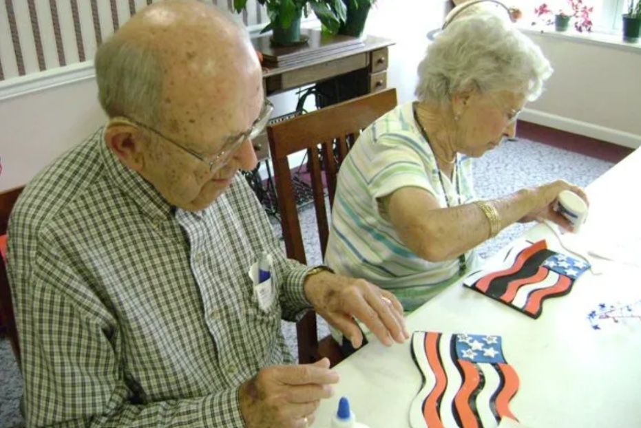 Two people painting paper flags at a table in a bright room