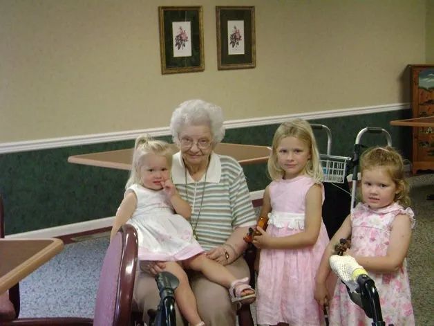 Elderly woman seated with three young children in a room with green walls and framed pictures