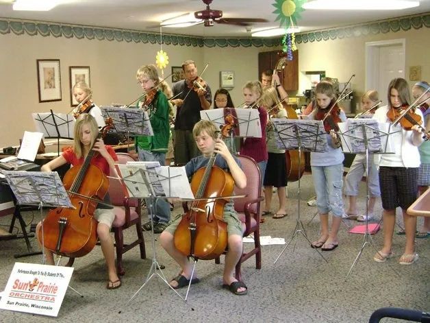 Children playing violins and cellos in a small indoor music recital room