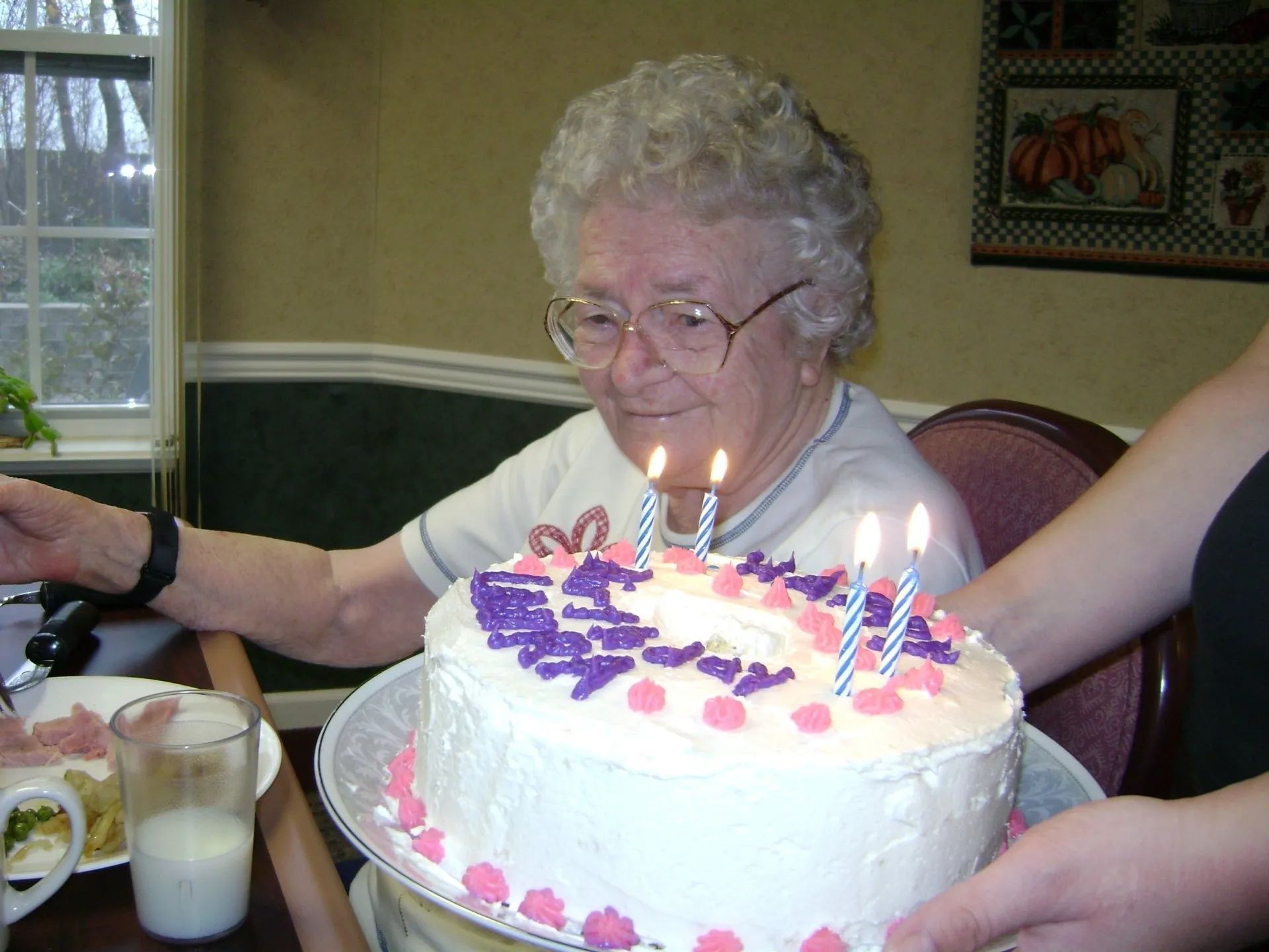 Woman smiling behind a birthday cake with lit candles at a table