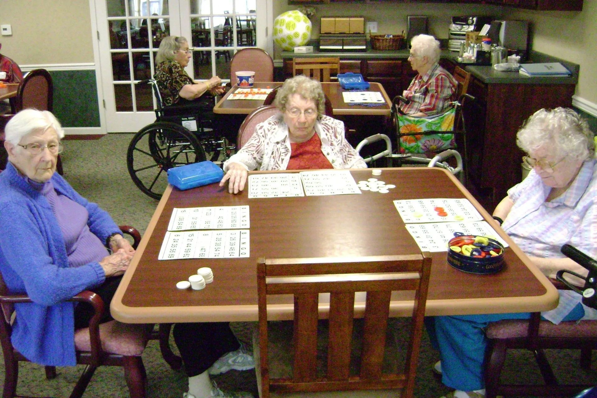 People playing a board game at a table in a living room, with a wheelchair nearby.