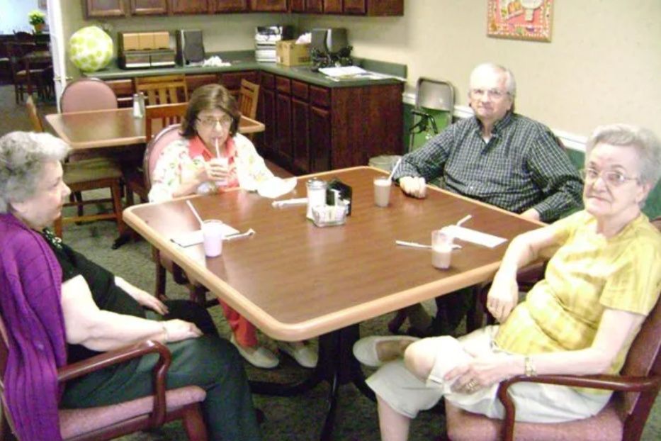 Four people sit around a table in a lounge, chatting over drinks and snacks.