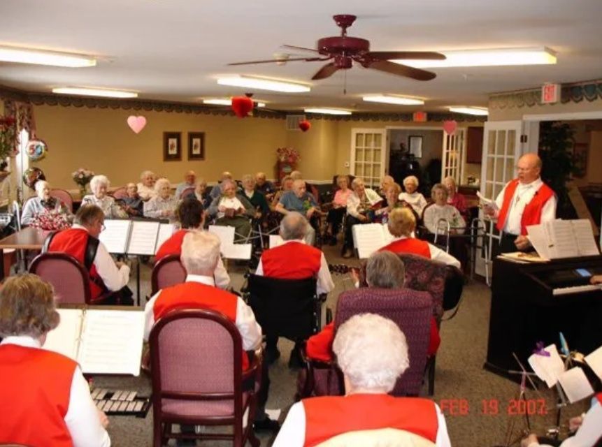 Musicians in red vests perform for a seated audience in a community room