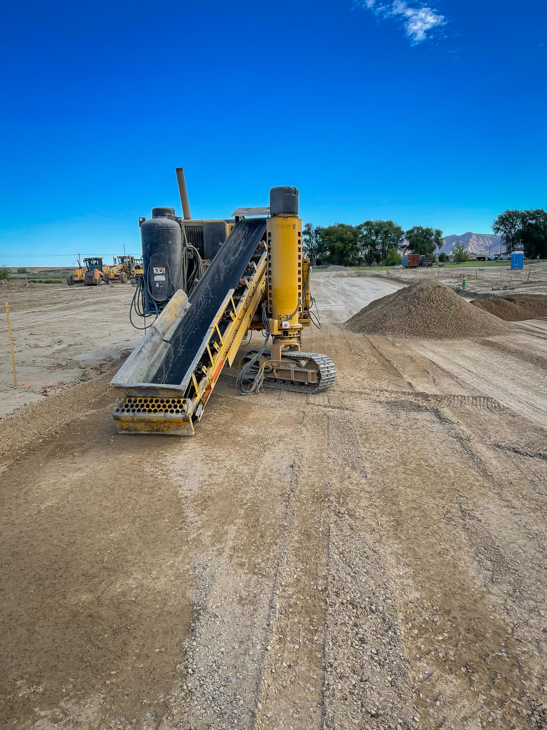 A yellow conveyor belt is sitting on top of a dirt road.
