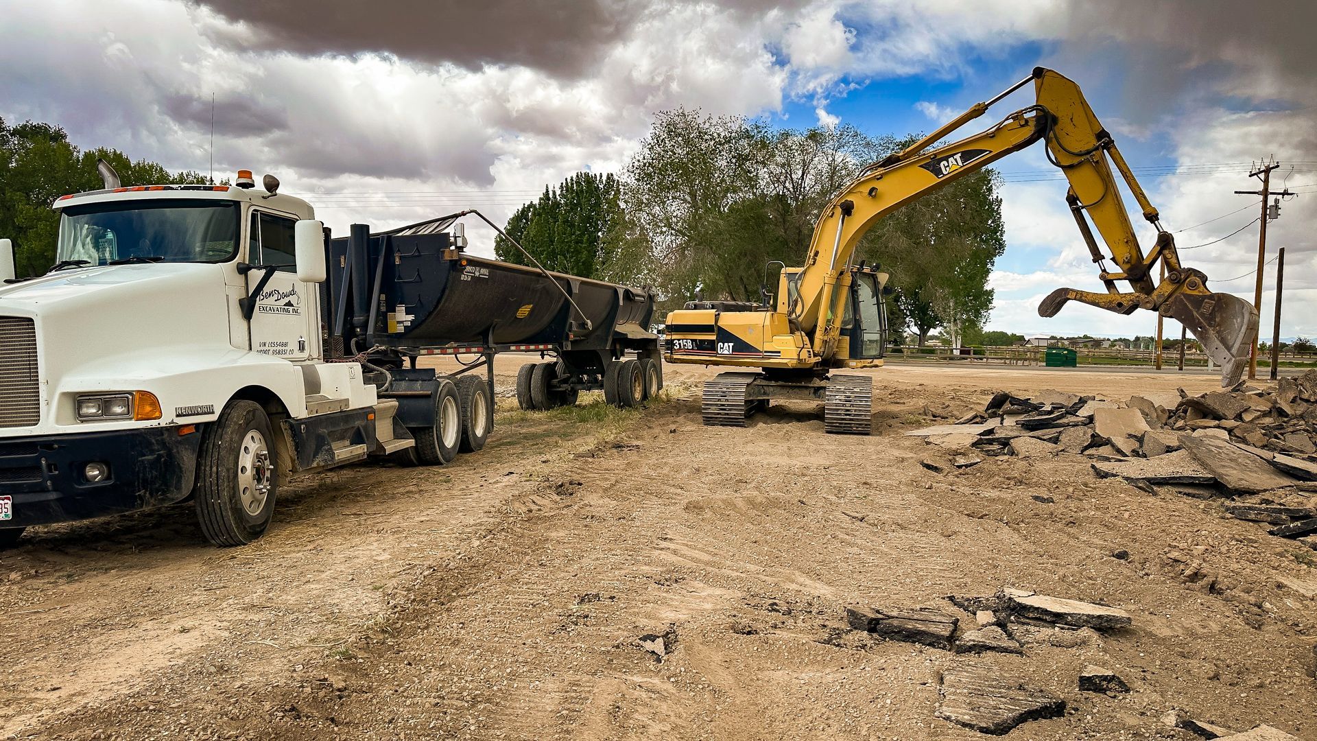 A truck is being towed by an excavator in a dirt field.