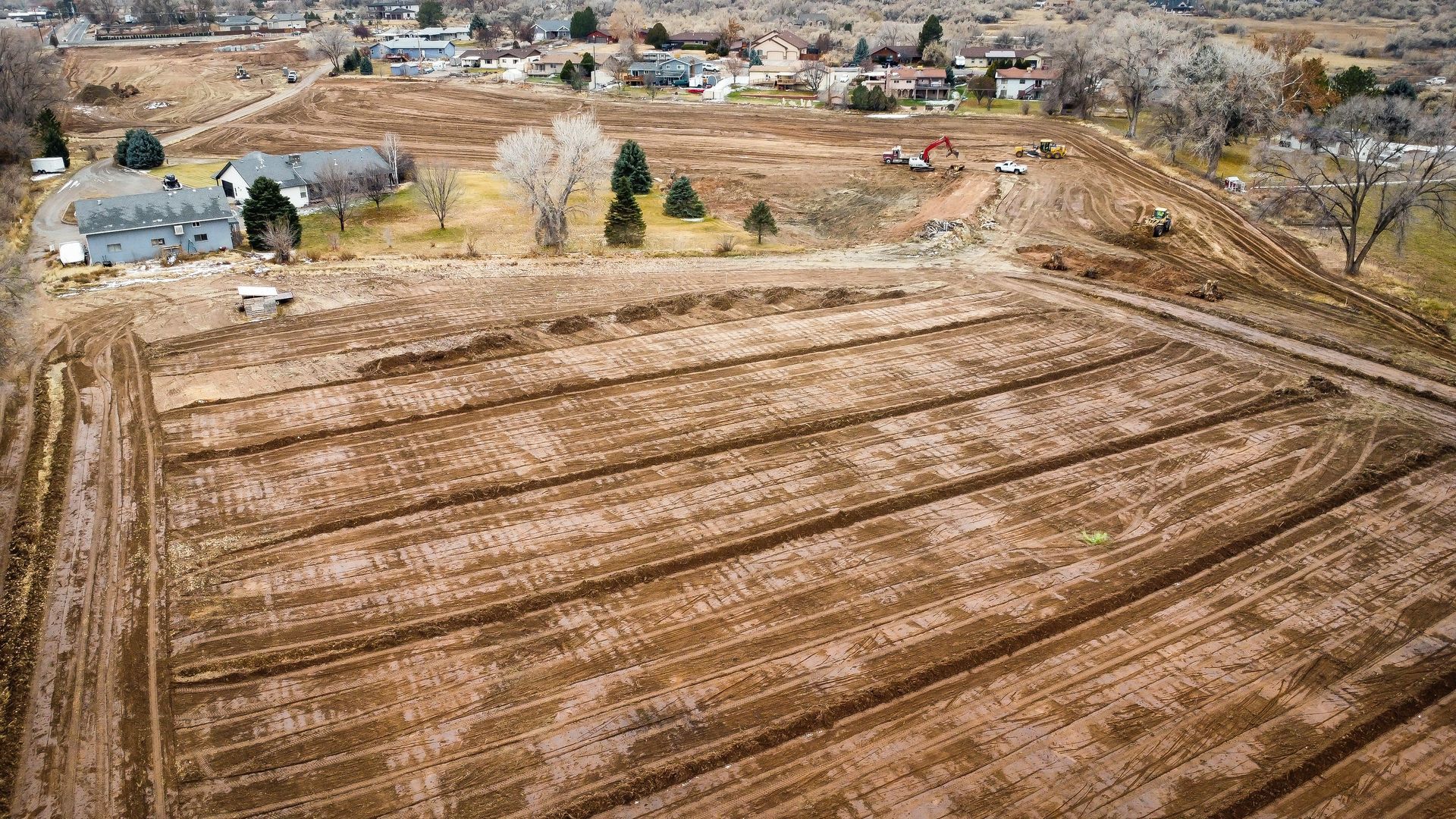 An aerial view of a dirt field with houses in the background.