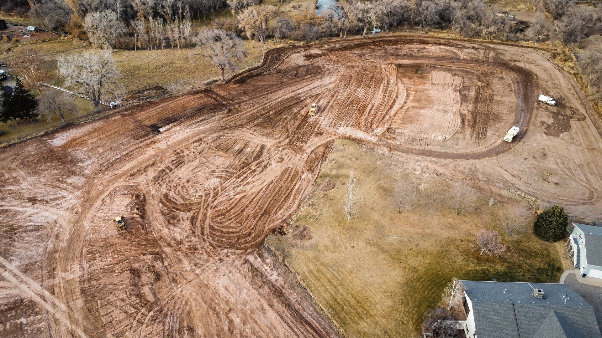 An aerial view of a large dirt field with a house in the background.