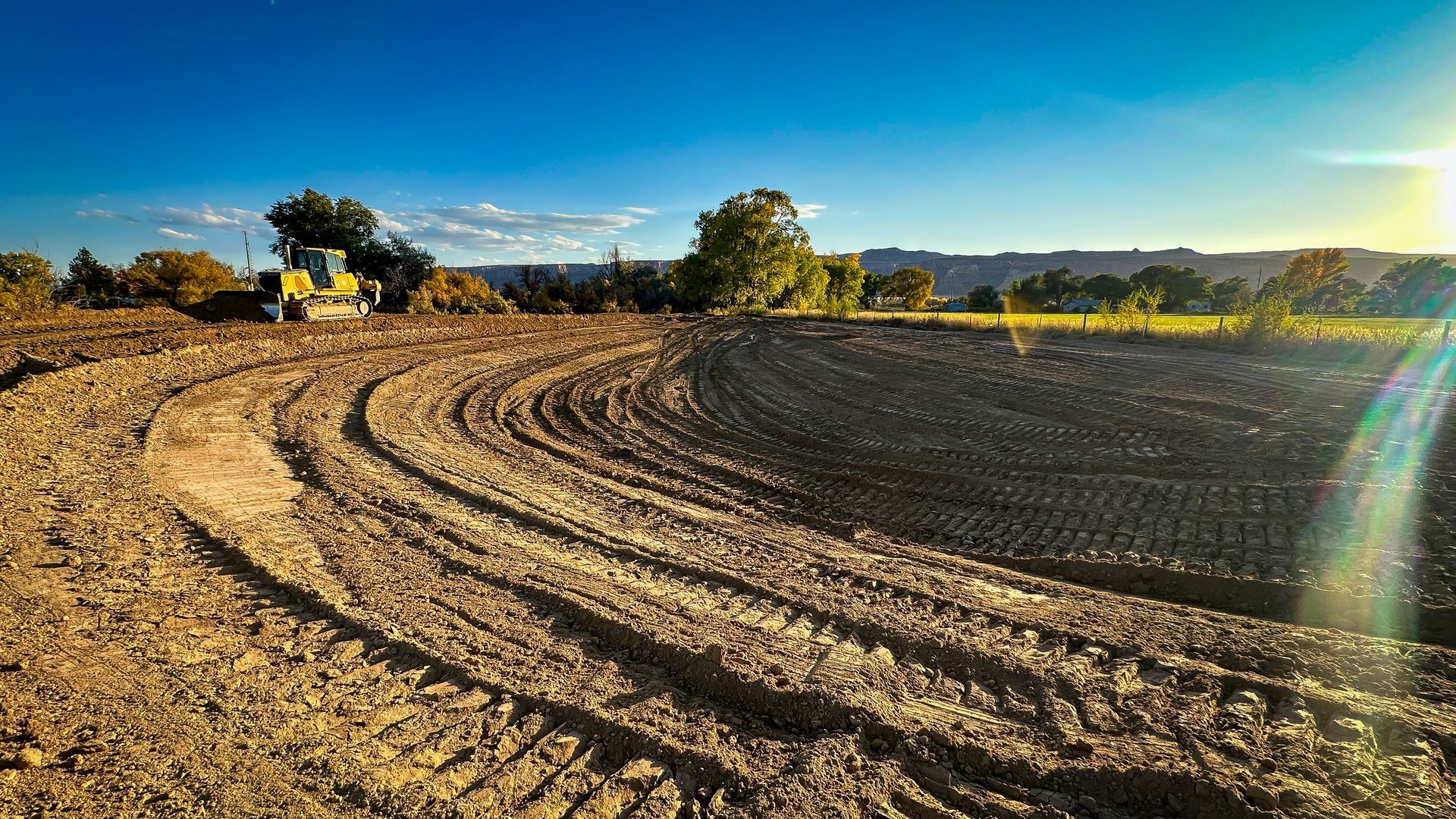 A bulldozer is plowing a dirt field at sunset.