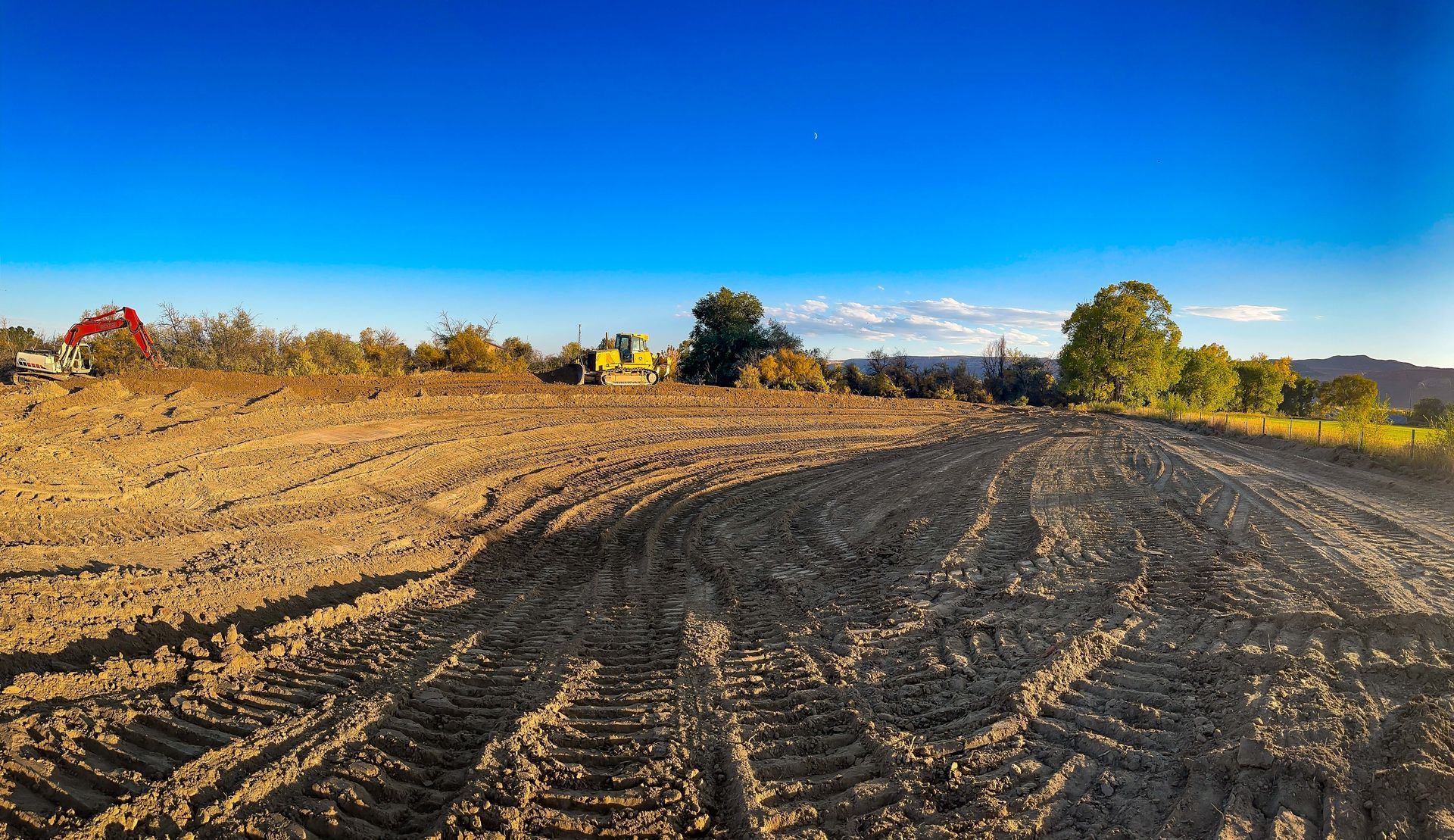 A dirt road going through a field with a blue sky in the background.