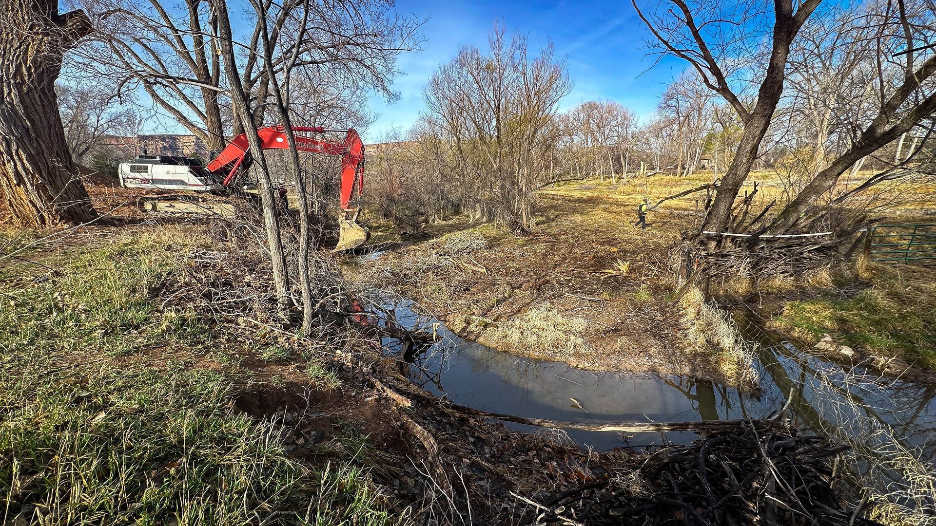 A red excavator is digging a hole in the middle of a river.