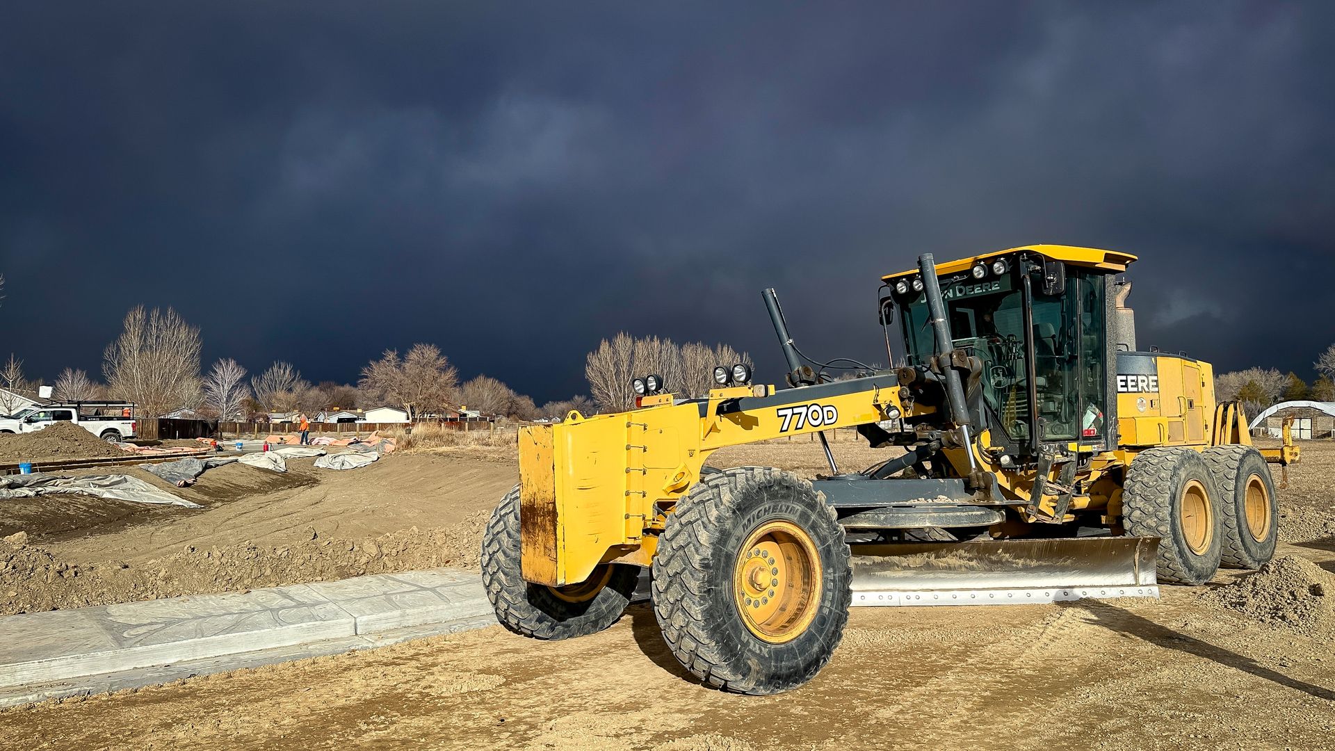 A yellow tractor is parked in a dirt field on a cloudy day.