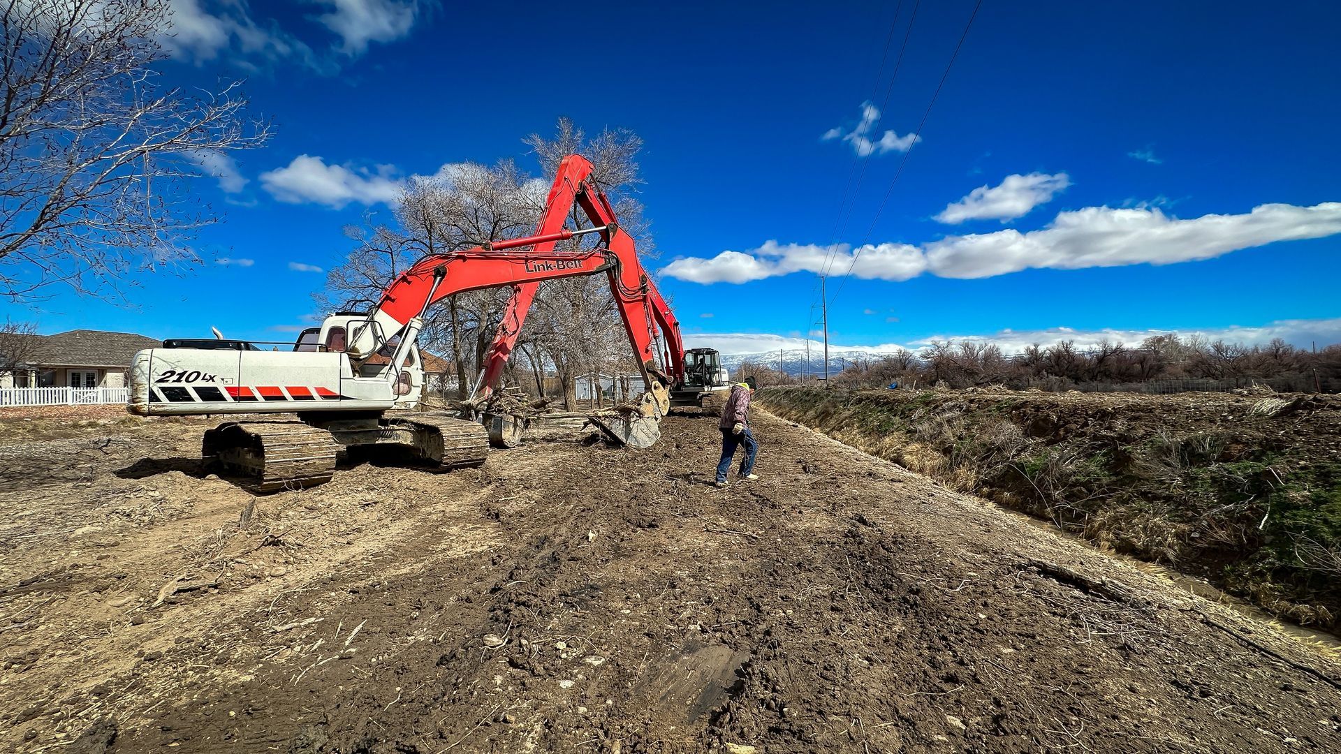 A man is standing next to a large excavator on a dirt road.