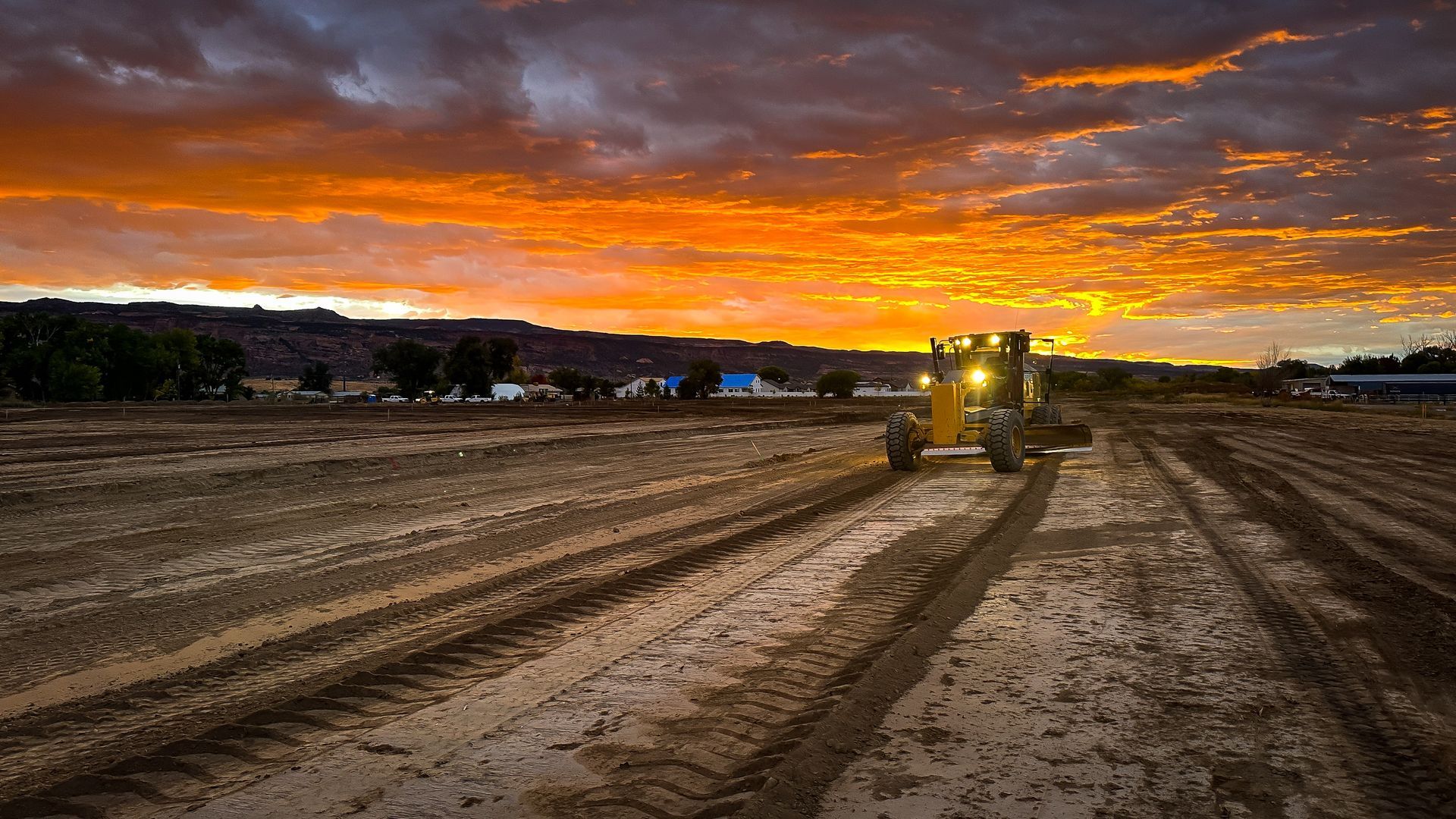 A tractor is plowing a muddy field at sunset.