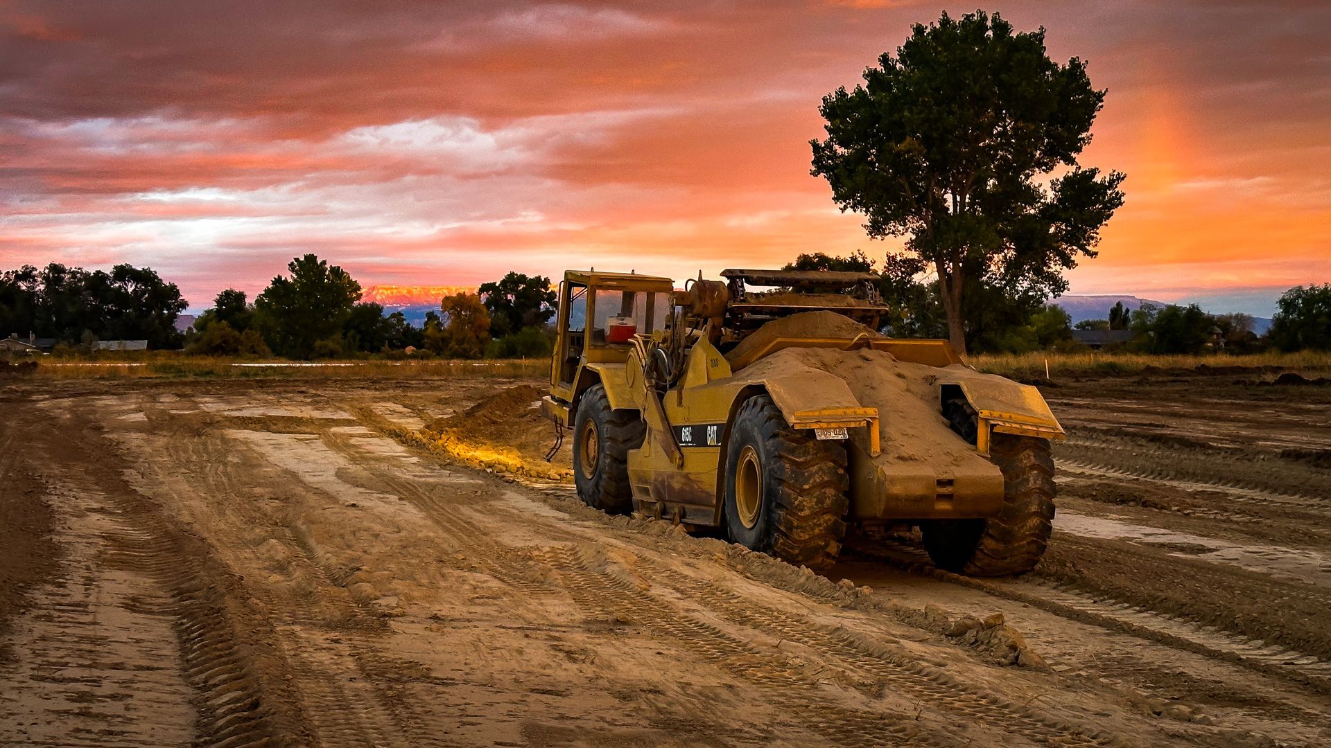 A bulldozer is driving down a dirt road at sunset.