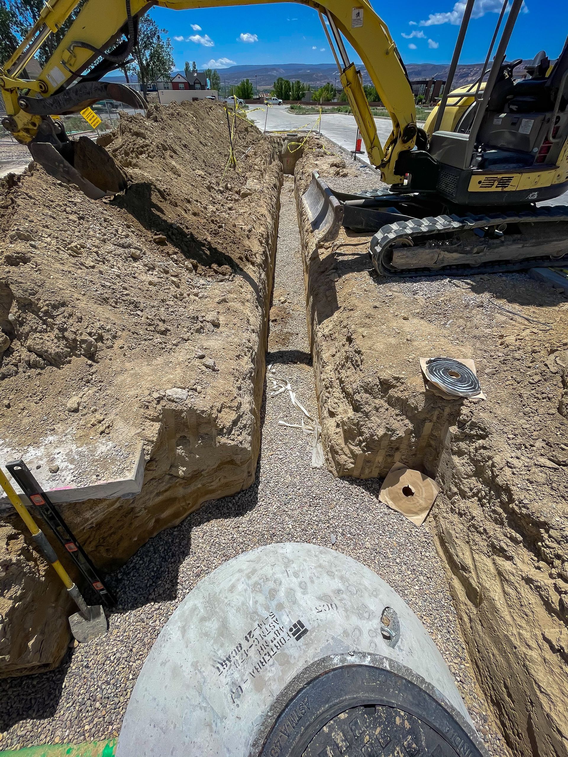 A yellow excavator is digging a trench in the dirt.