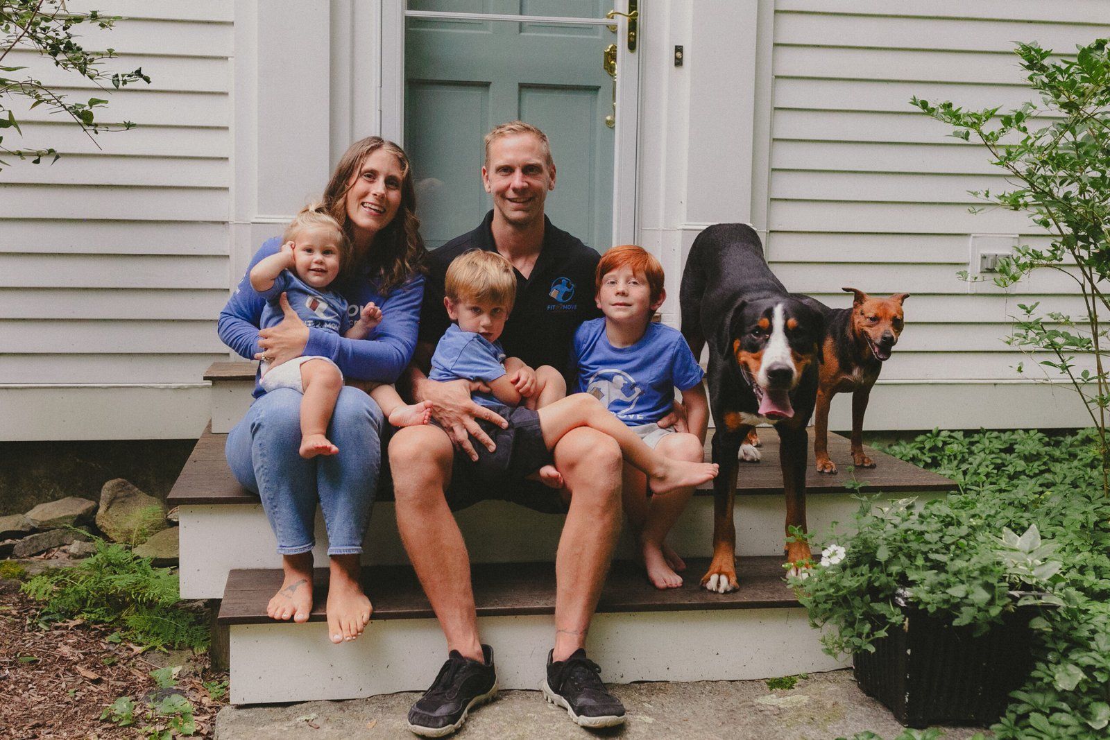 Family of five and two dogs sitting on porch steps.