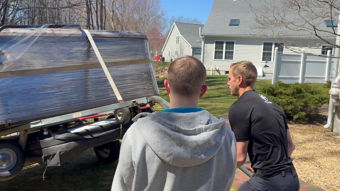 Two men unloading a large wrapped object from a truck in a backyard.
