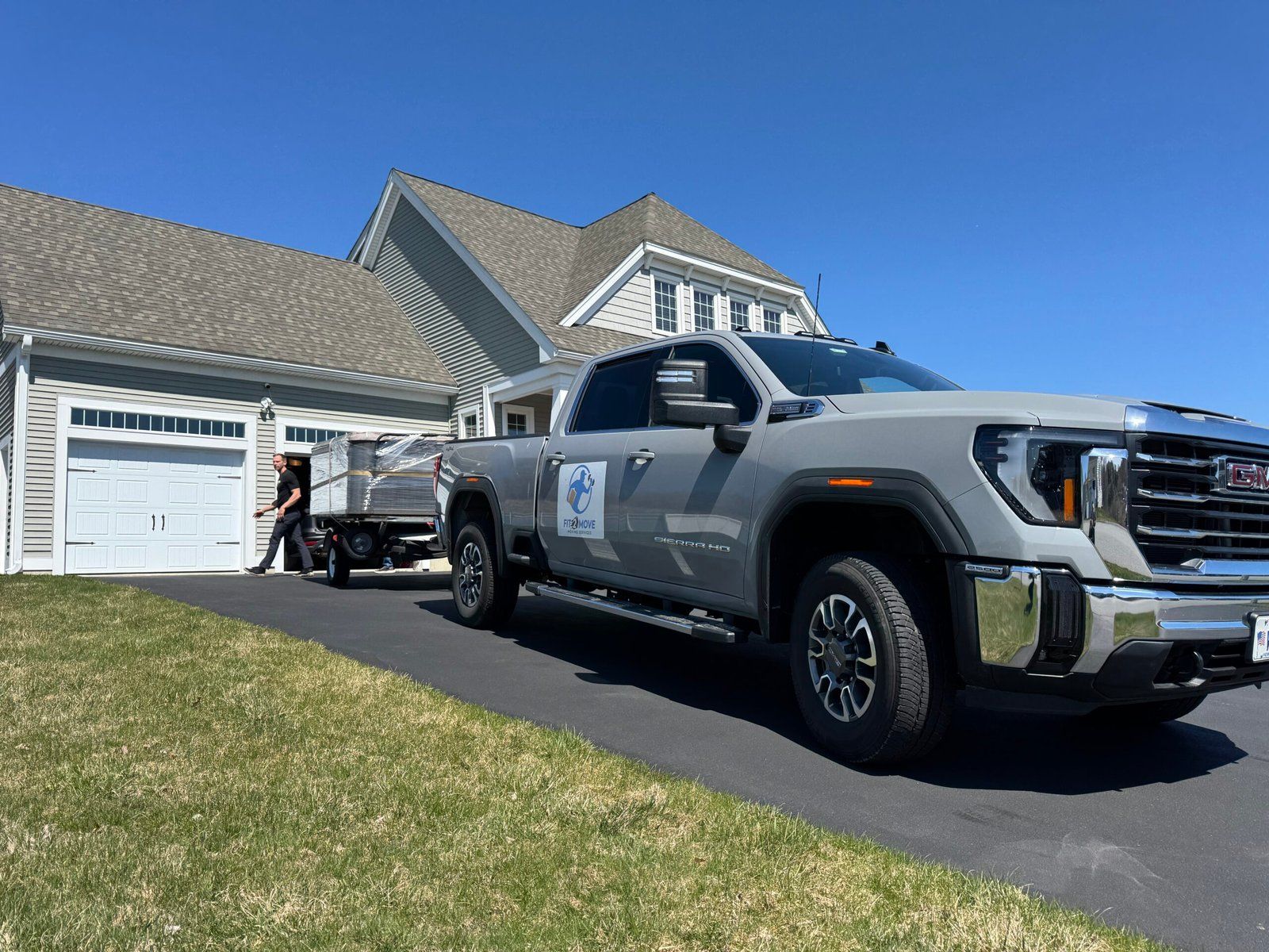Gray pickup truck with a trailer parked in a driveway next to a house; person by trailer.