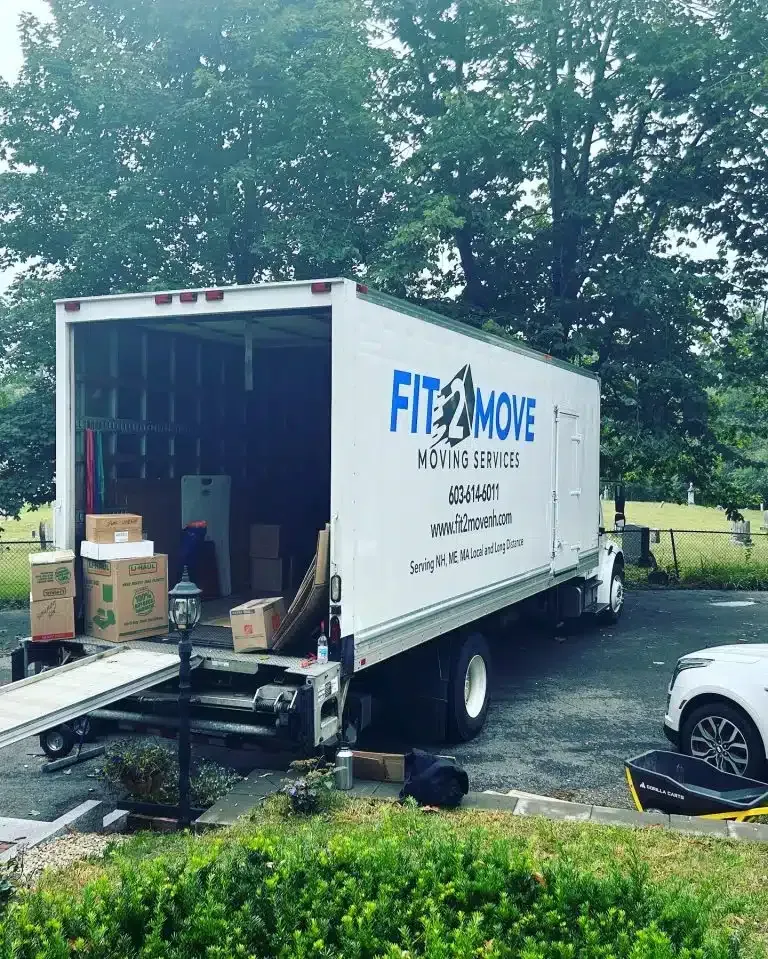 Moving truck open, boxes and a refrigerator inside. The truck is parked outside a home.