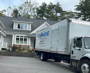 Moving truck parked in front of a gray house, the logo for