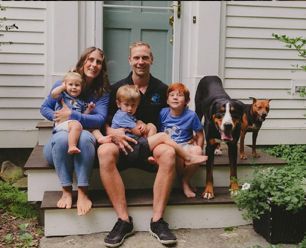 Family sitting on front steps with three children and two dogs.