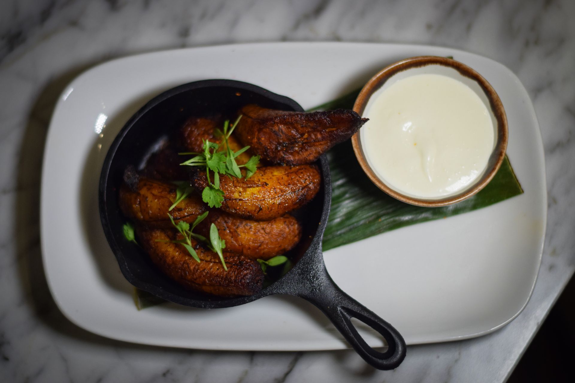 A white plate topped with fried plantains and a bowl of sour cream.