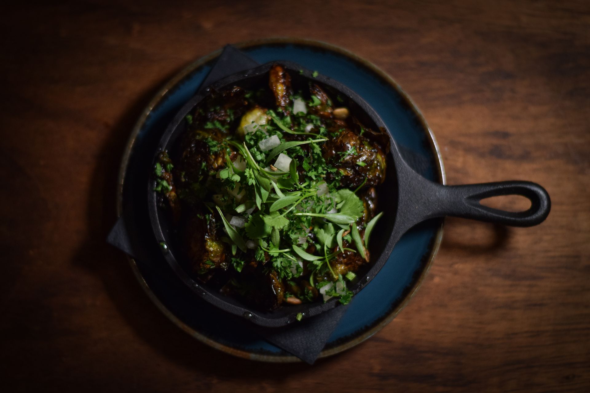 A skillet filled with vegetables is on a plate on a wooden table.