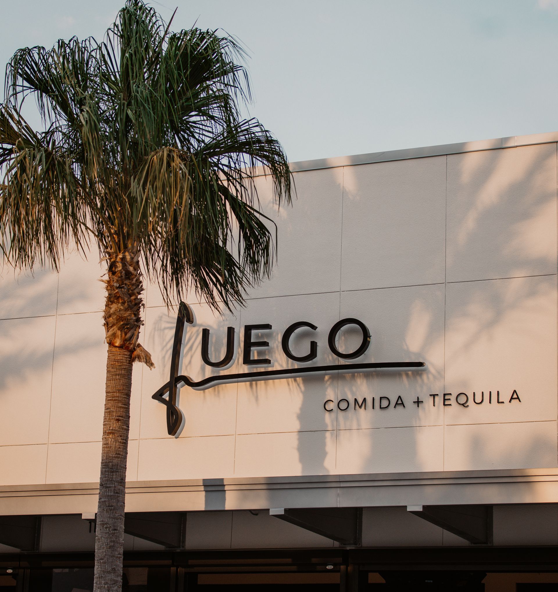 A sign for fuego comida tequila with a palm tree in front of it