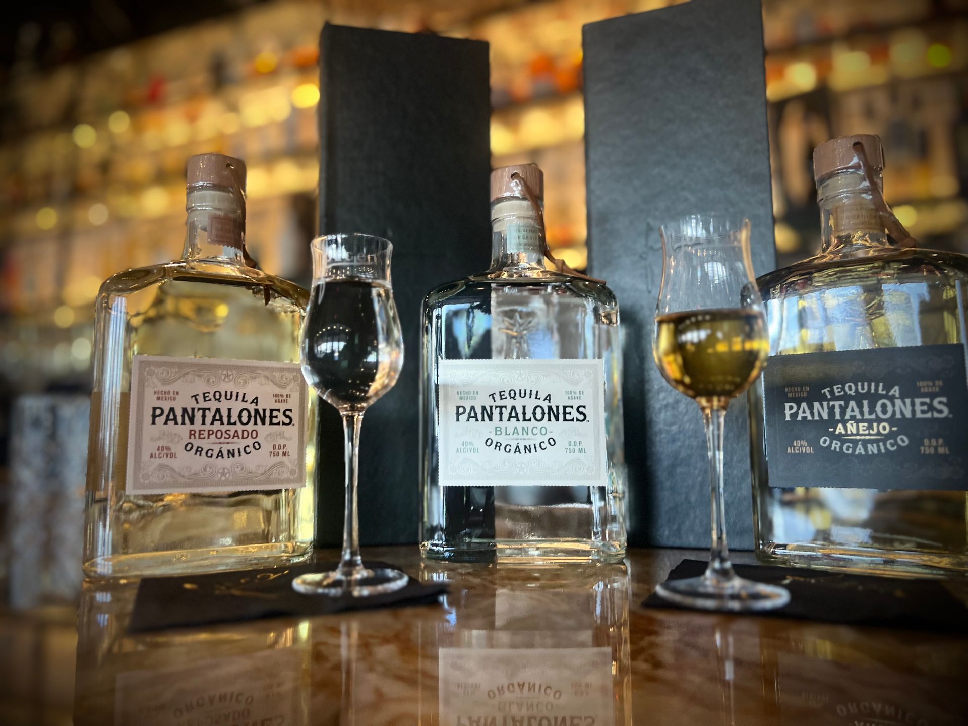 Three bottles of tequila and two glasses of wine are on a table.