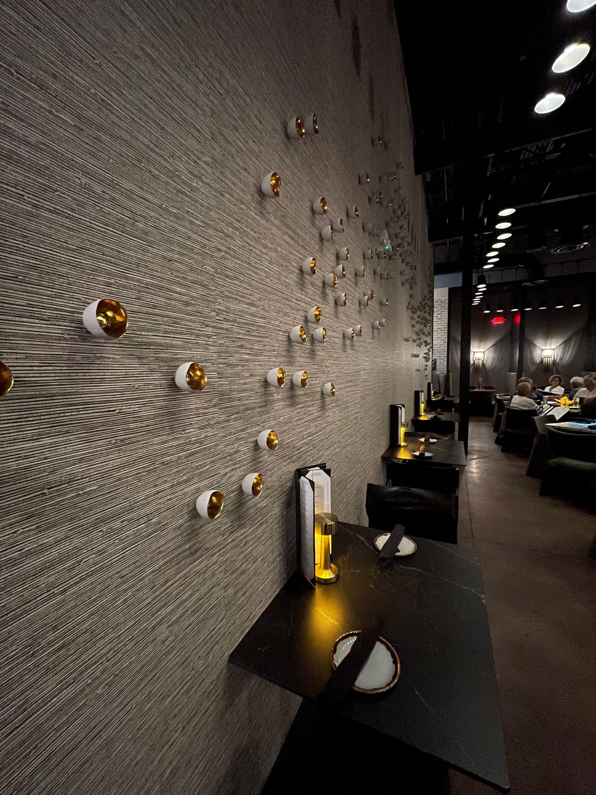 A restaurant with tables and chairs in front of a wall with candles on it.