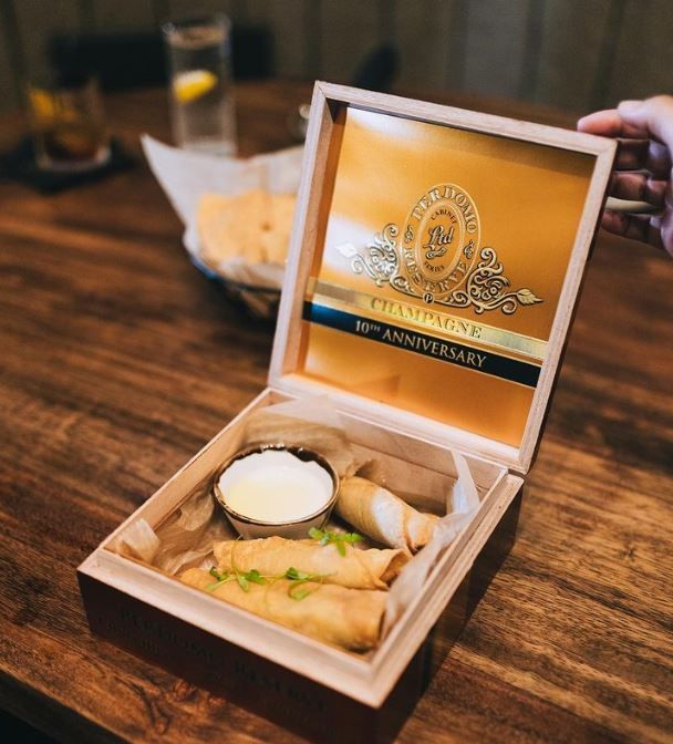 A person is holding a box of food on a wooden table