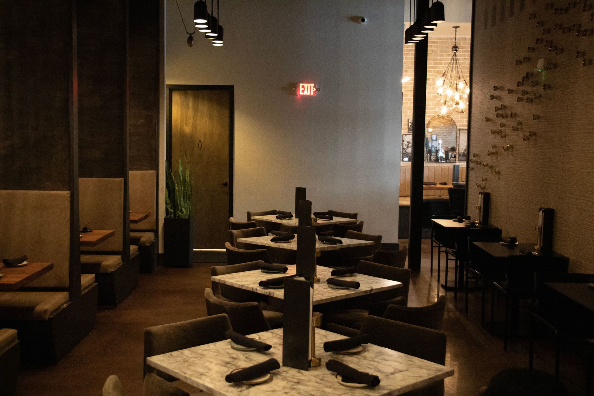 A restaurant with tables and chairs and a red exit sign.