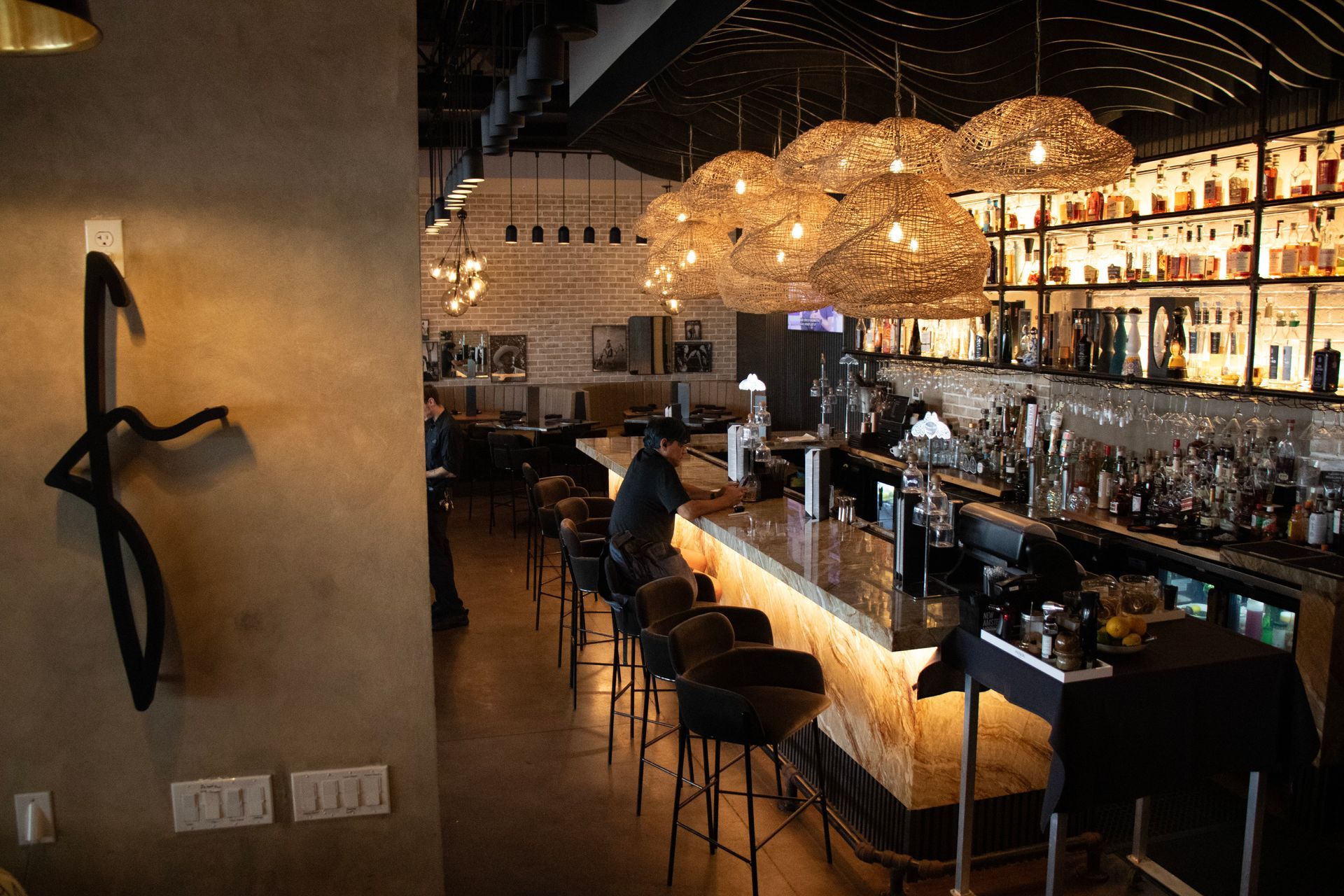 A restaurant with a long bar and a few people sitting at the bar.