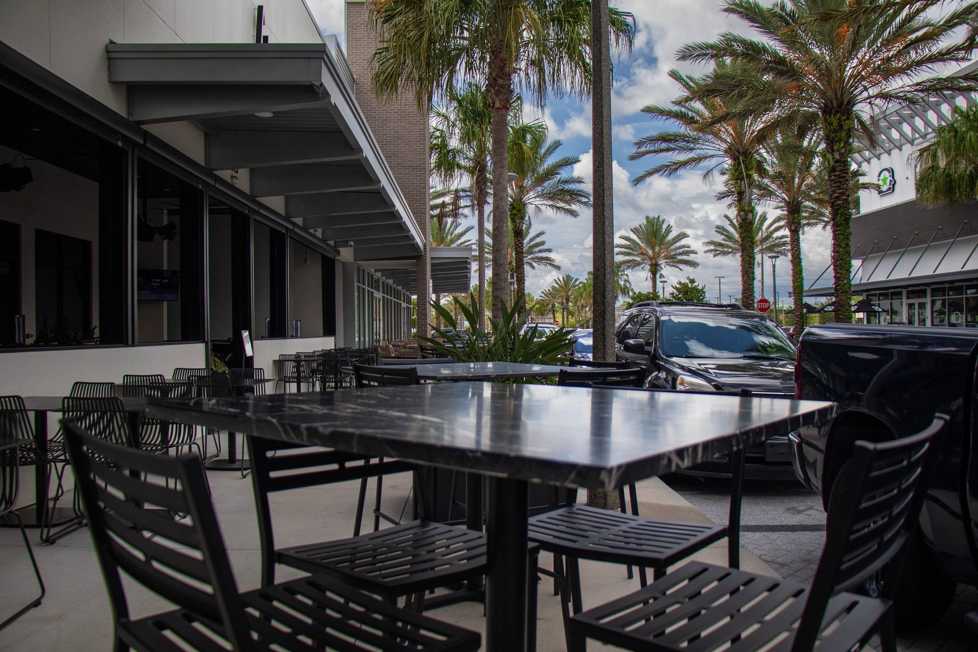 A patio with tables and chairs in front of a building with palm trees.