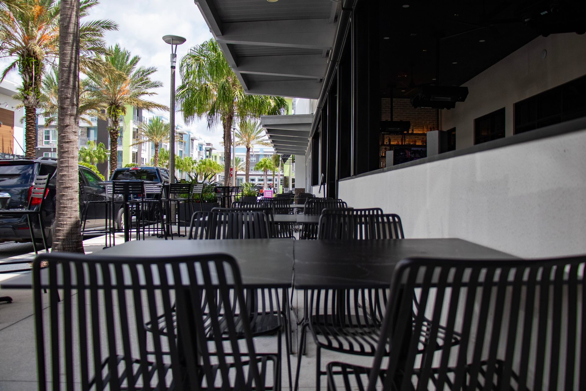 A restaurant with tables and chairs outside with palm trees in the background.