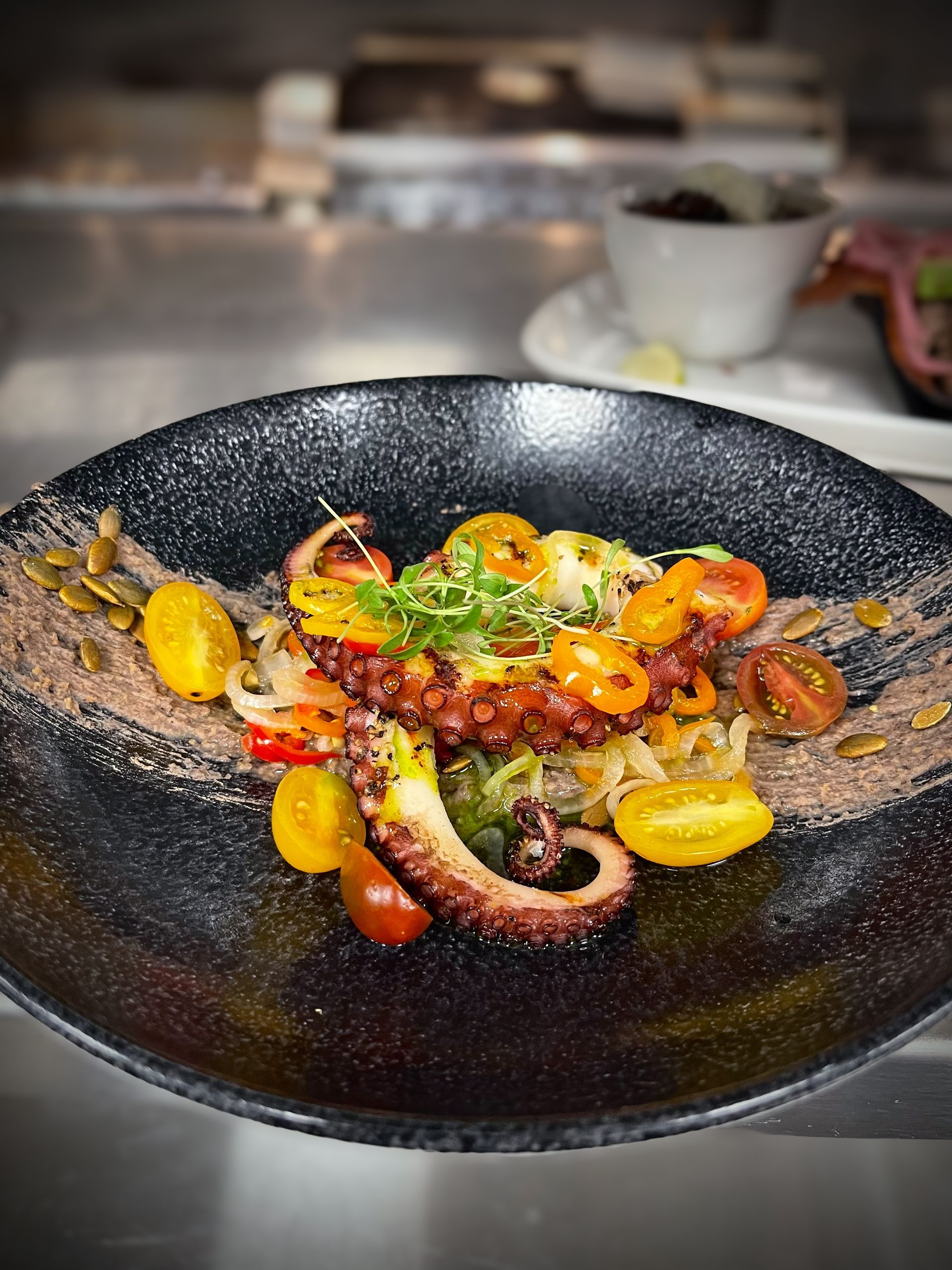 A close up of a plate of food with octopus and tomatoes on a table.
